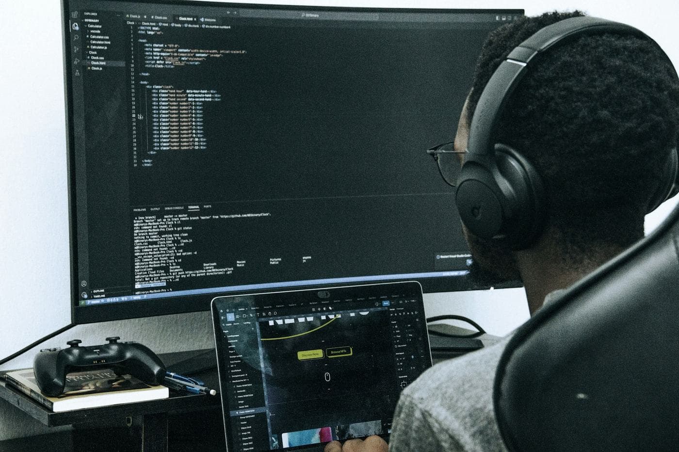 Un développeur, casque sur les oreilles, travaille devant un grand écran et un ordinateur portable