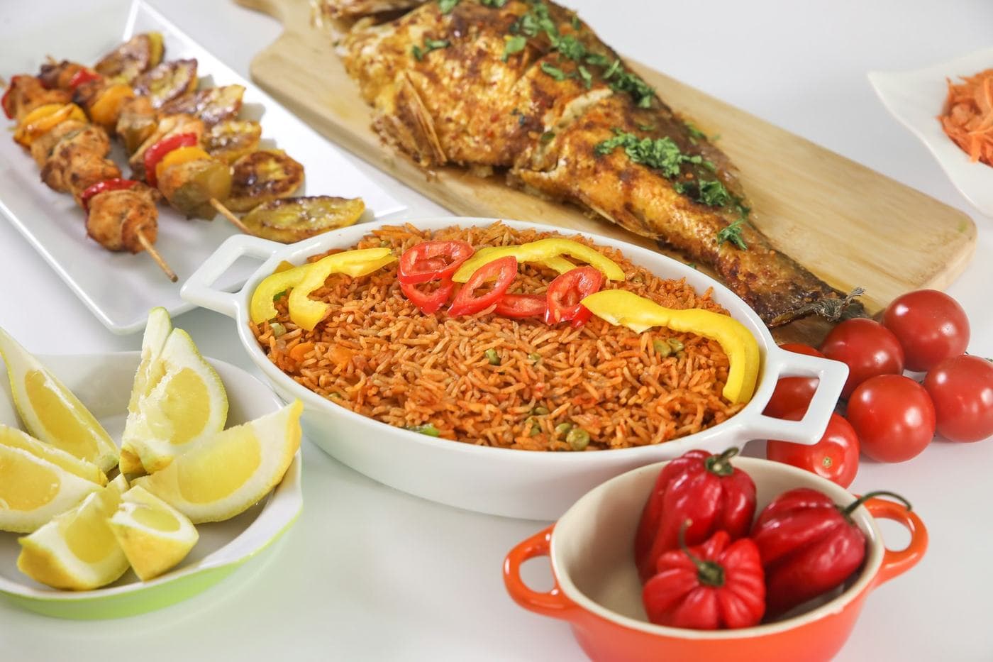 Plat de riz rouge aux poivrons, poisson grillé entier, brochettes, tomates et citrons