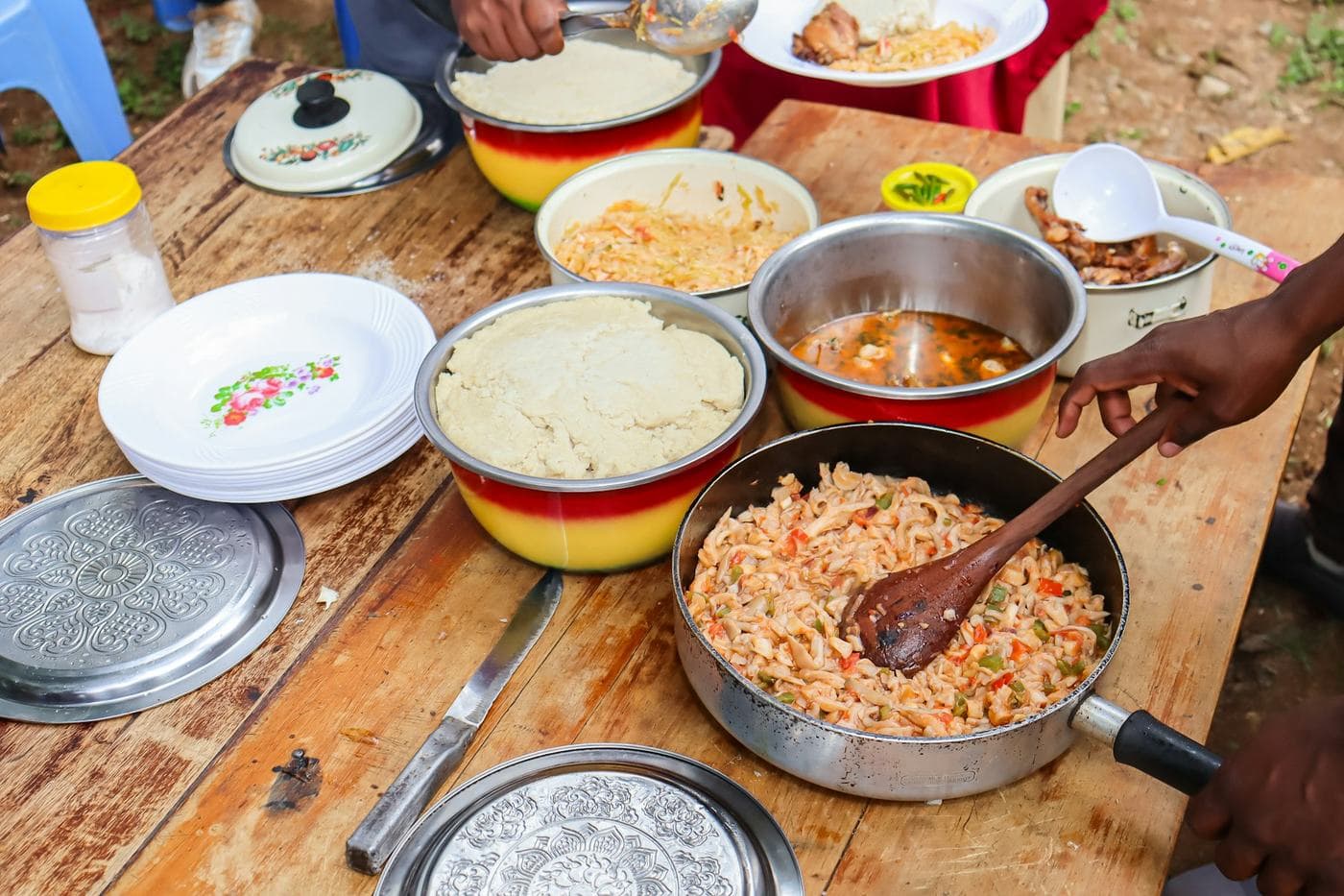 Marmites et plats préparés sur une table en bois, une main sert une assiette